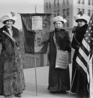 3 women standing with voting sign and flag