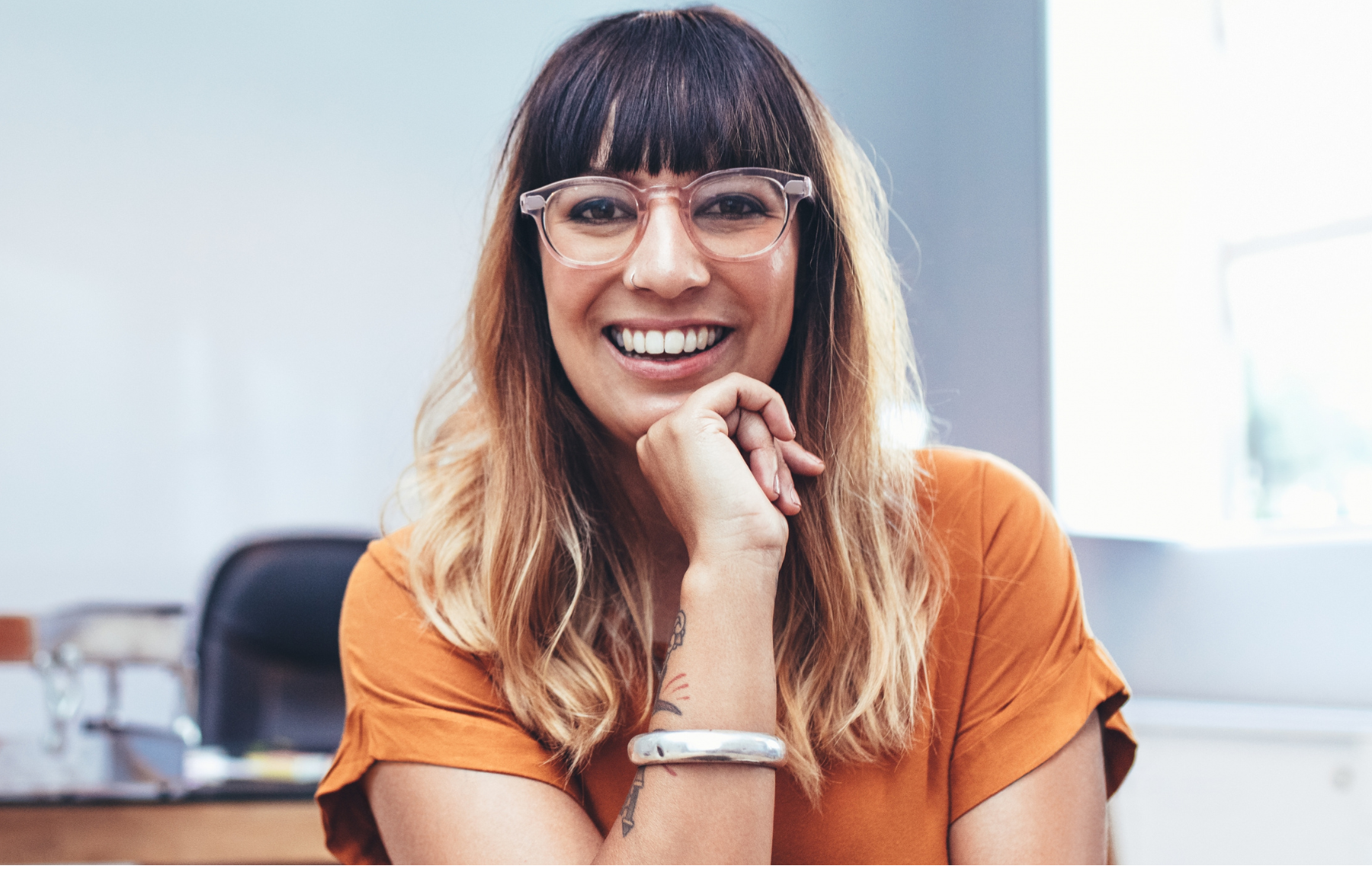 girl with glasses and tattoo holding hand by chin smiling