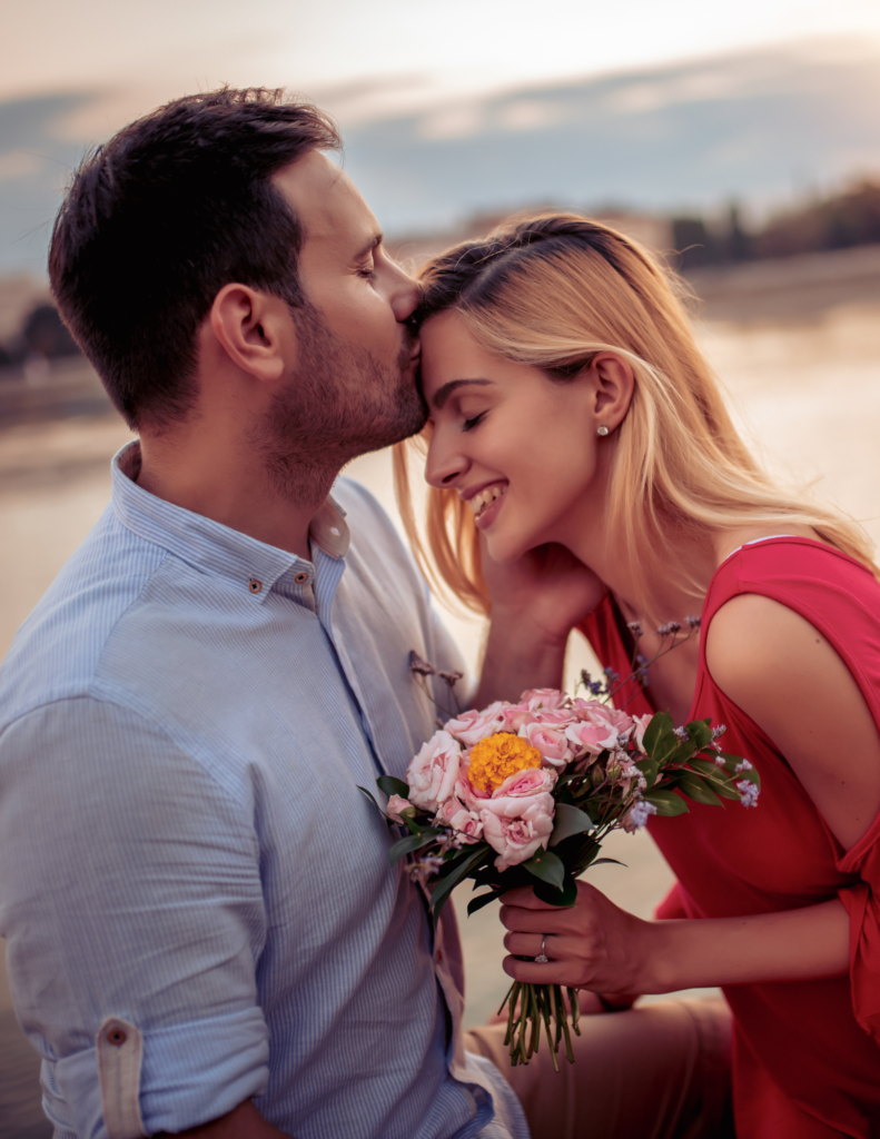 Man kissing wife's head. Wife holding flowers