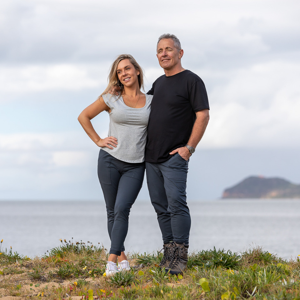 man and woman hug with ocean in background