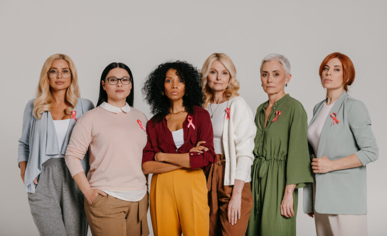 Group of confident mature women wearing breast cancer ribbons against grey background