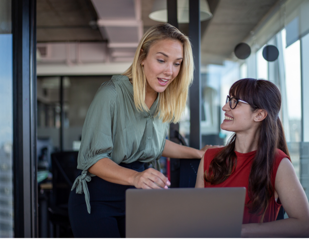 Woman talking with another woman working on computer