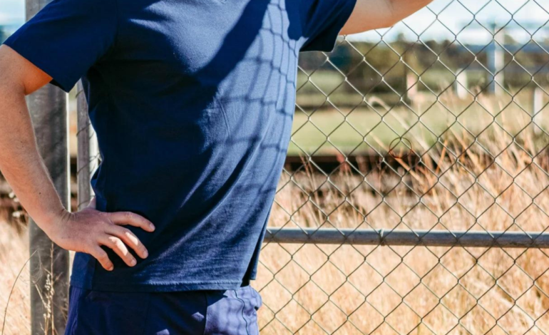 Mens blue shirt and shorts hand on fence