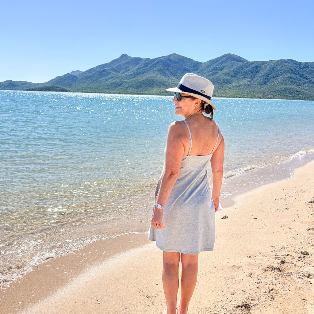 woman in gray dress on beach facing away from camera looking over shoulder