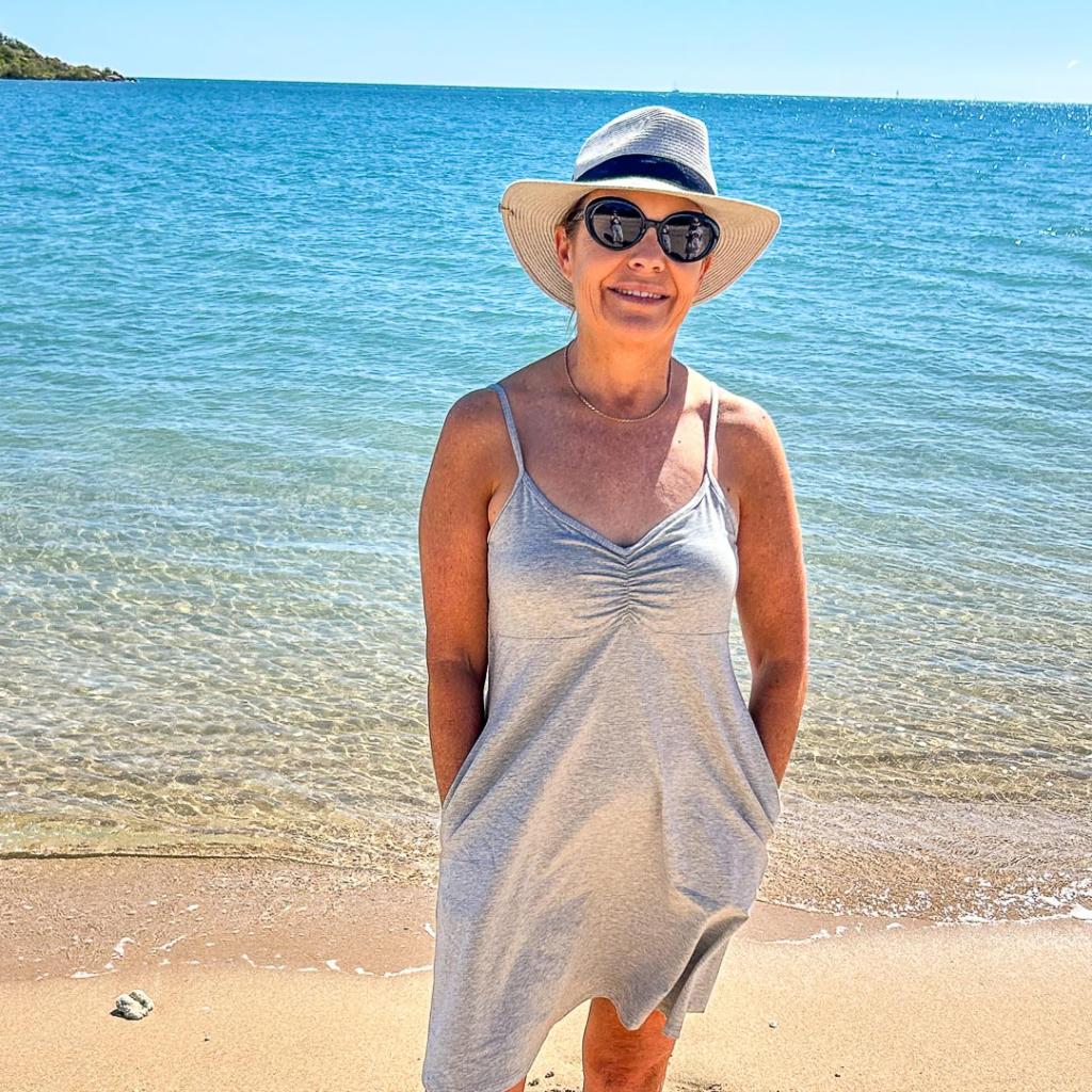 smiling woman in gray dress on beach with hands in pockets