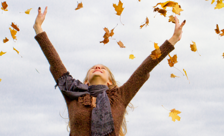 woman throwing hands up in the air with leaves up in the air as well