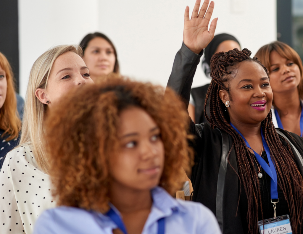 Women at conference and one black woman holding hand up