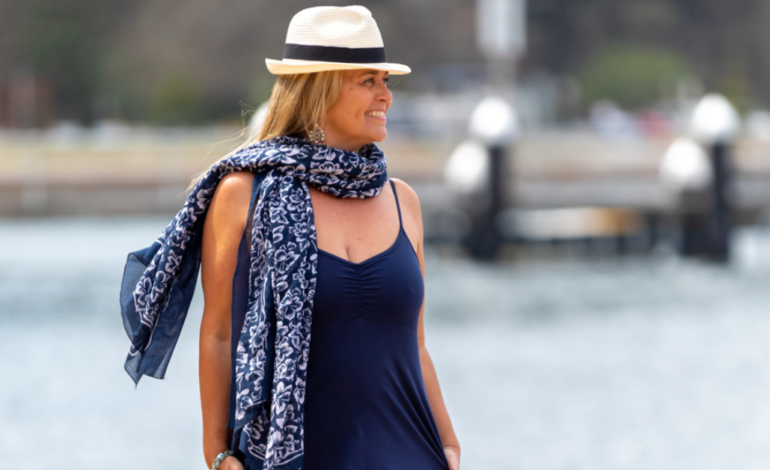 smiling woman walking next to ocean with hat and scarf