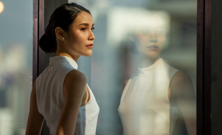 business woman looking out city building window at reflection