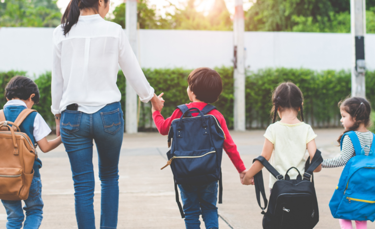 woman holding hands with kids walking into school