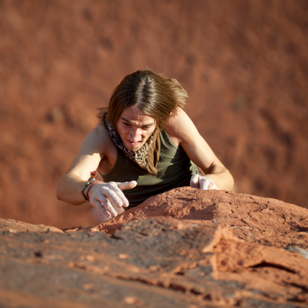 woman free climbing up tall red rock