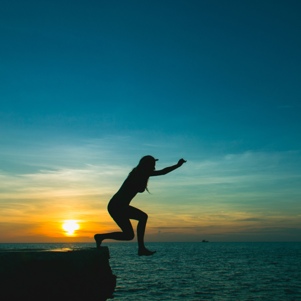 woman jumping off cliff into water