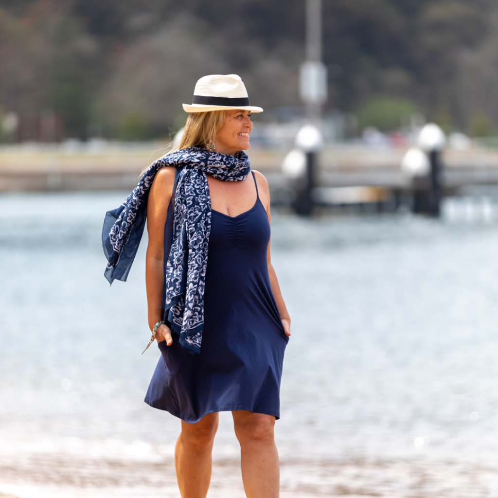 happy woman in blue dress walking next to beach smiling