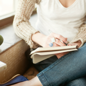 woman  with legs crossed writing in a notebook