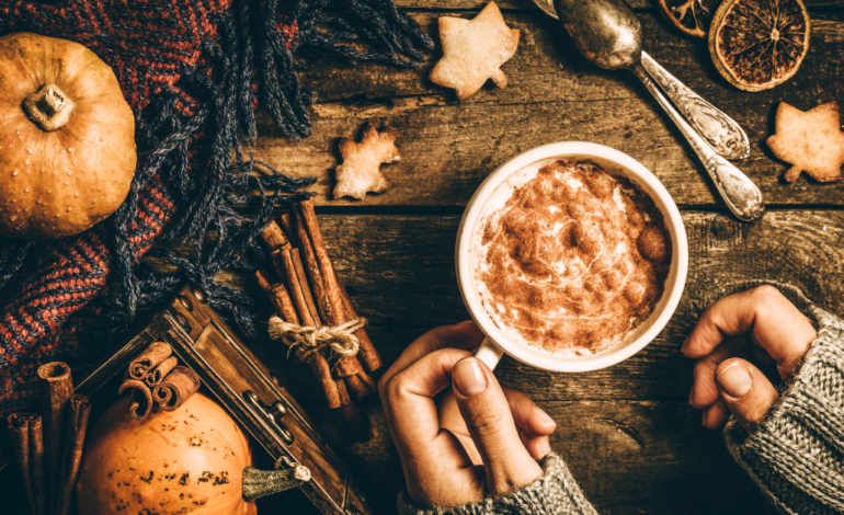 photo of woman holding fall drink in mug on wooden table