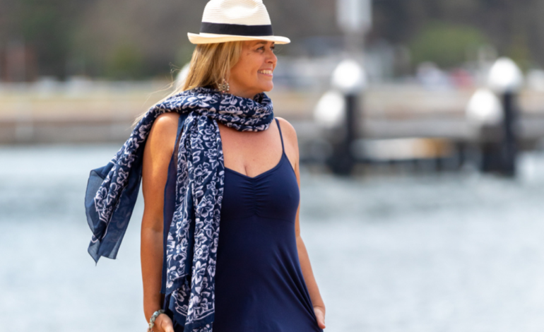 smiling woman walking down beach wearing hat and scarf