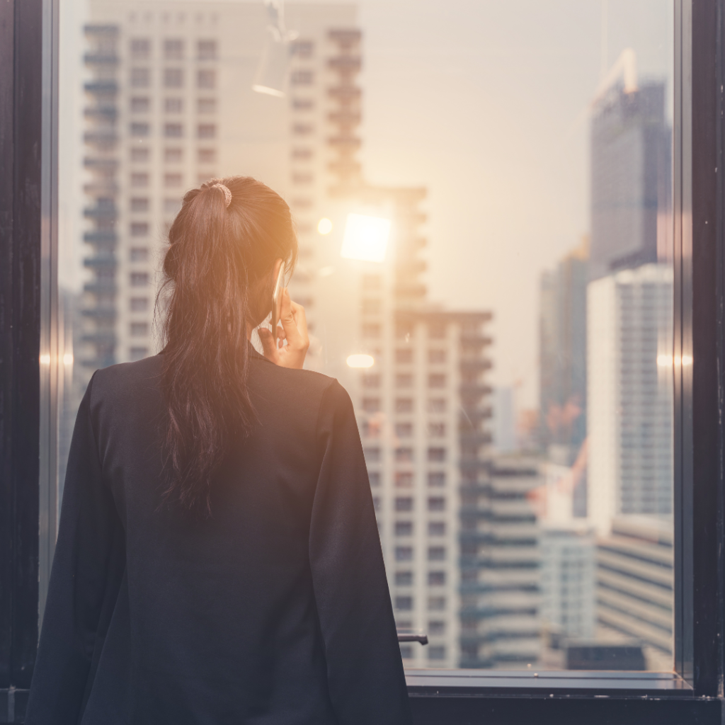 business woman looking out high rise city window on phone