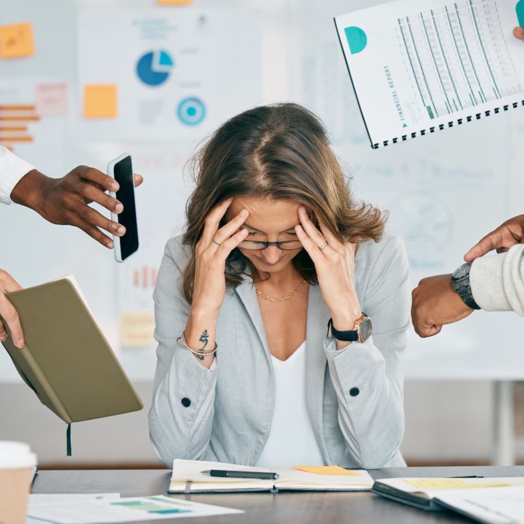 corporate woman overwhelmed at desk with hands coming at her