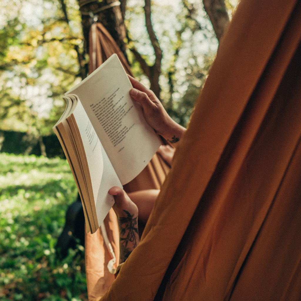 woman laying in hammock in forest reading a book