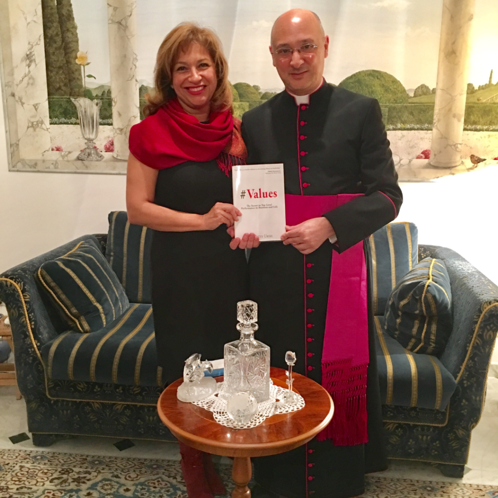 Betty Uribe holding book "#Values" next to priest