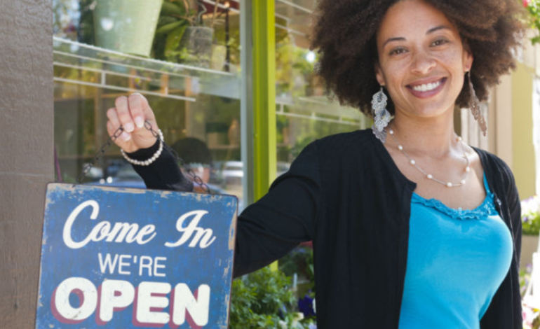 female small business owner holding "open" sign in window