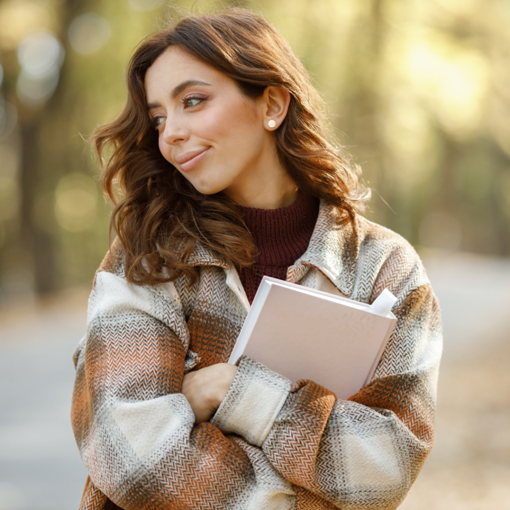 girl in plaid coat holding book in autumn forest