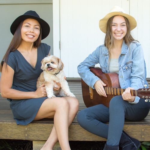 2 girls sitting with a dog and one with a guitar