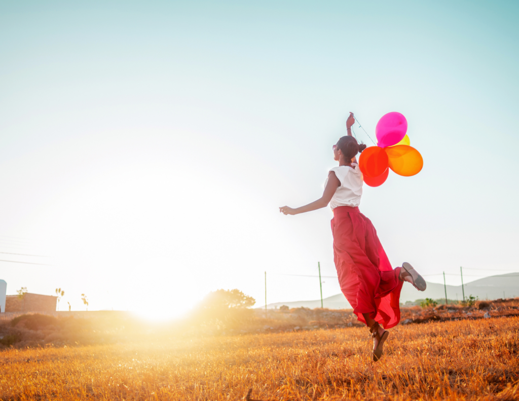 Women in field jumping with balloons in hand