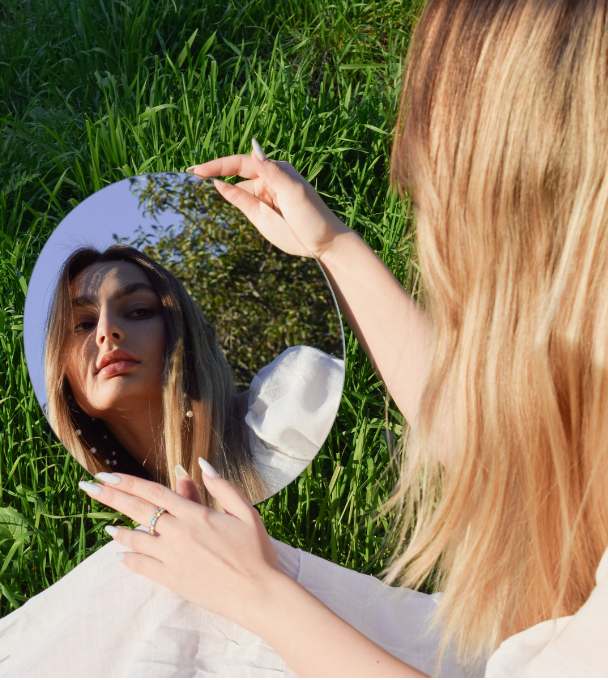 Woman looking at herself in mirror sitting on grass