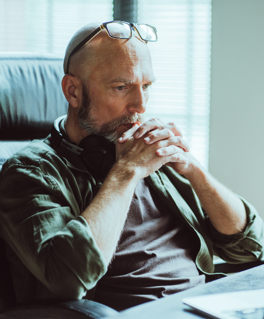 man with hands clasped and glasses on head sitting at desk