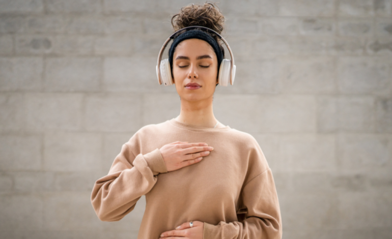 Young female with headphones on and hand on chest meditating